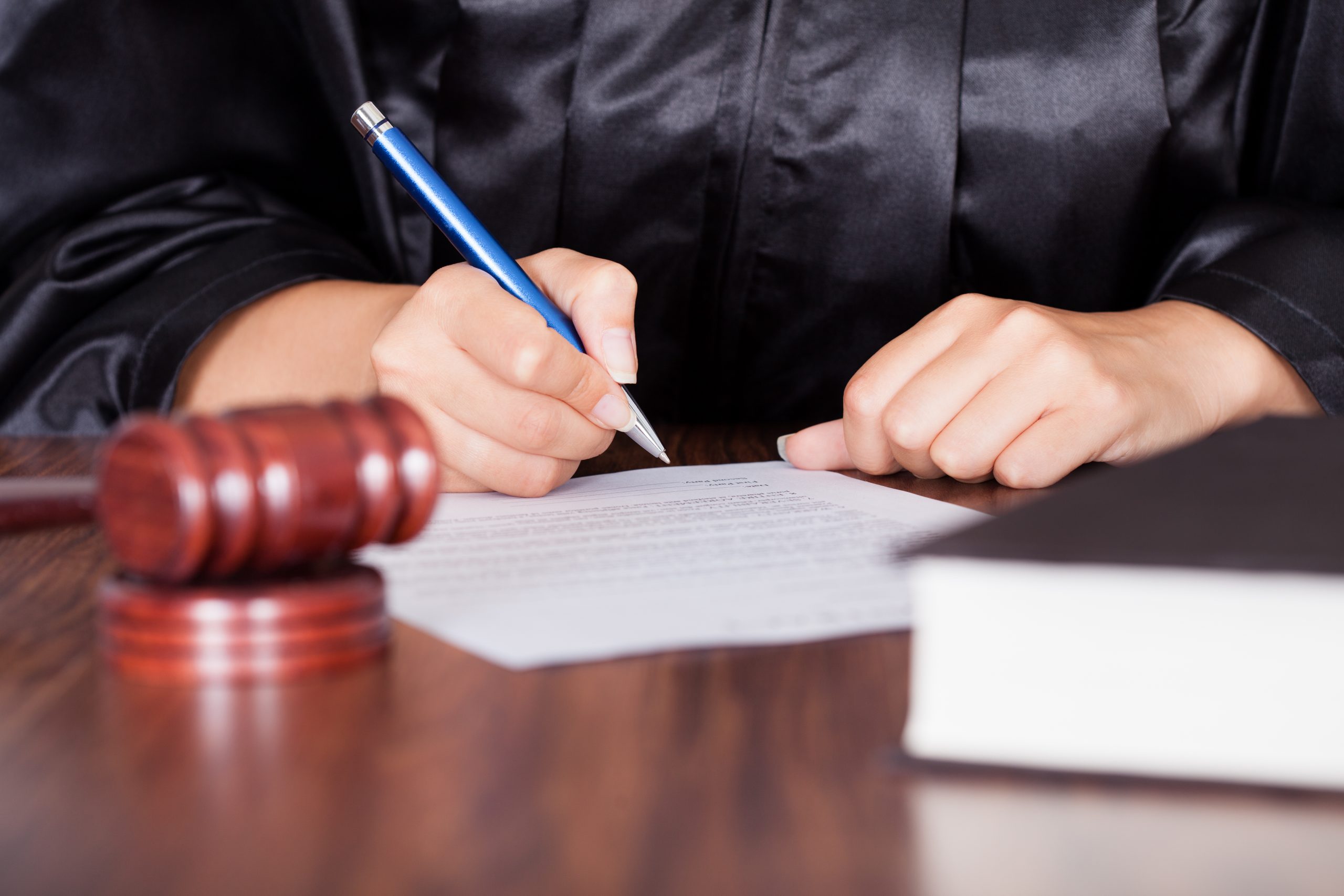 Close-up Of Female Hand Writing On Paper In Courtroom