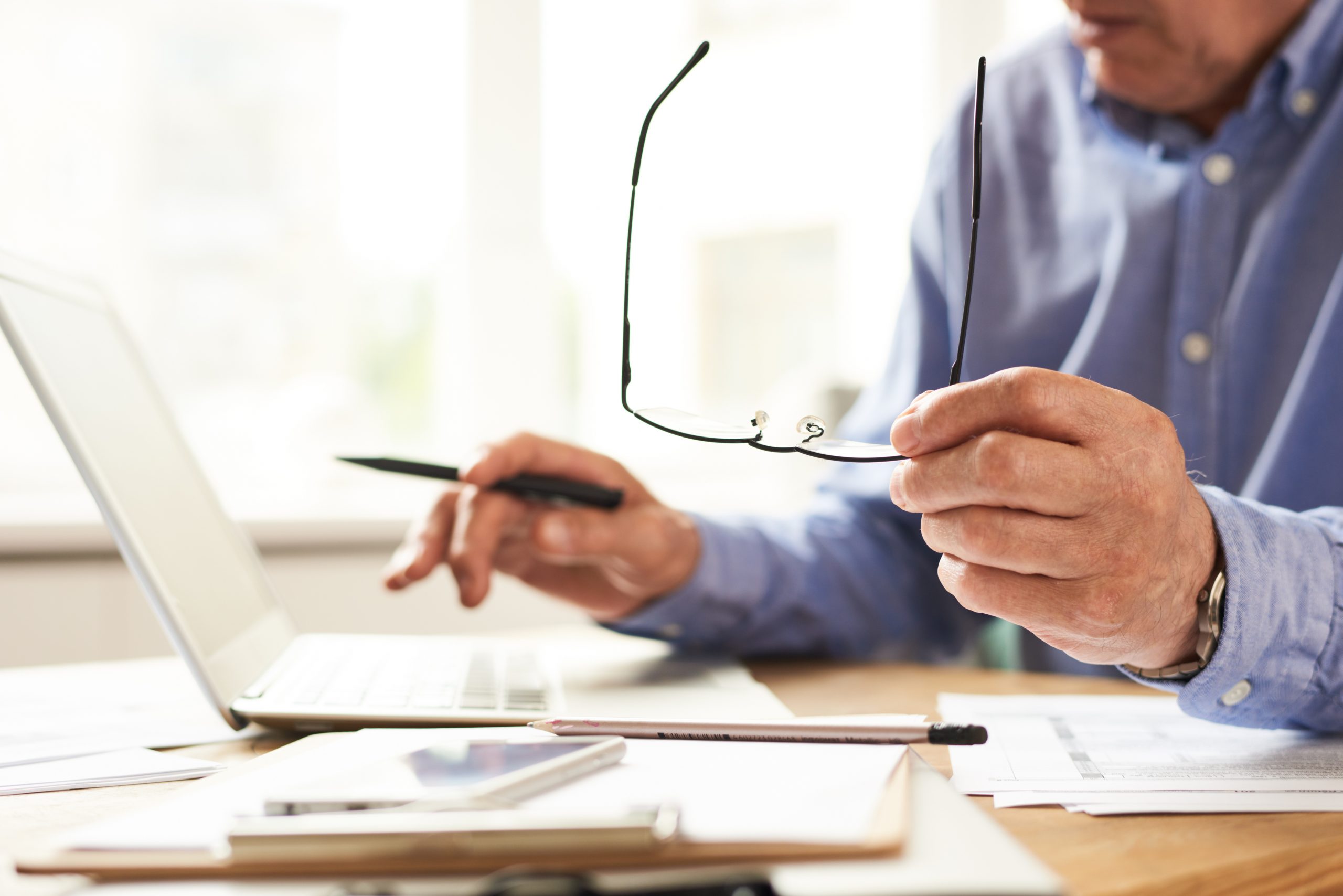 Closeup  of unrecognizable senior man filling in typing working with laptop at home and holding glasses in hand
