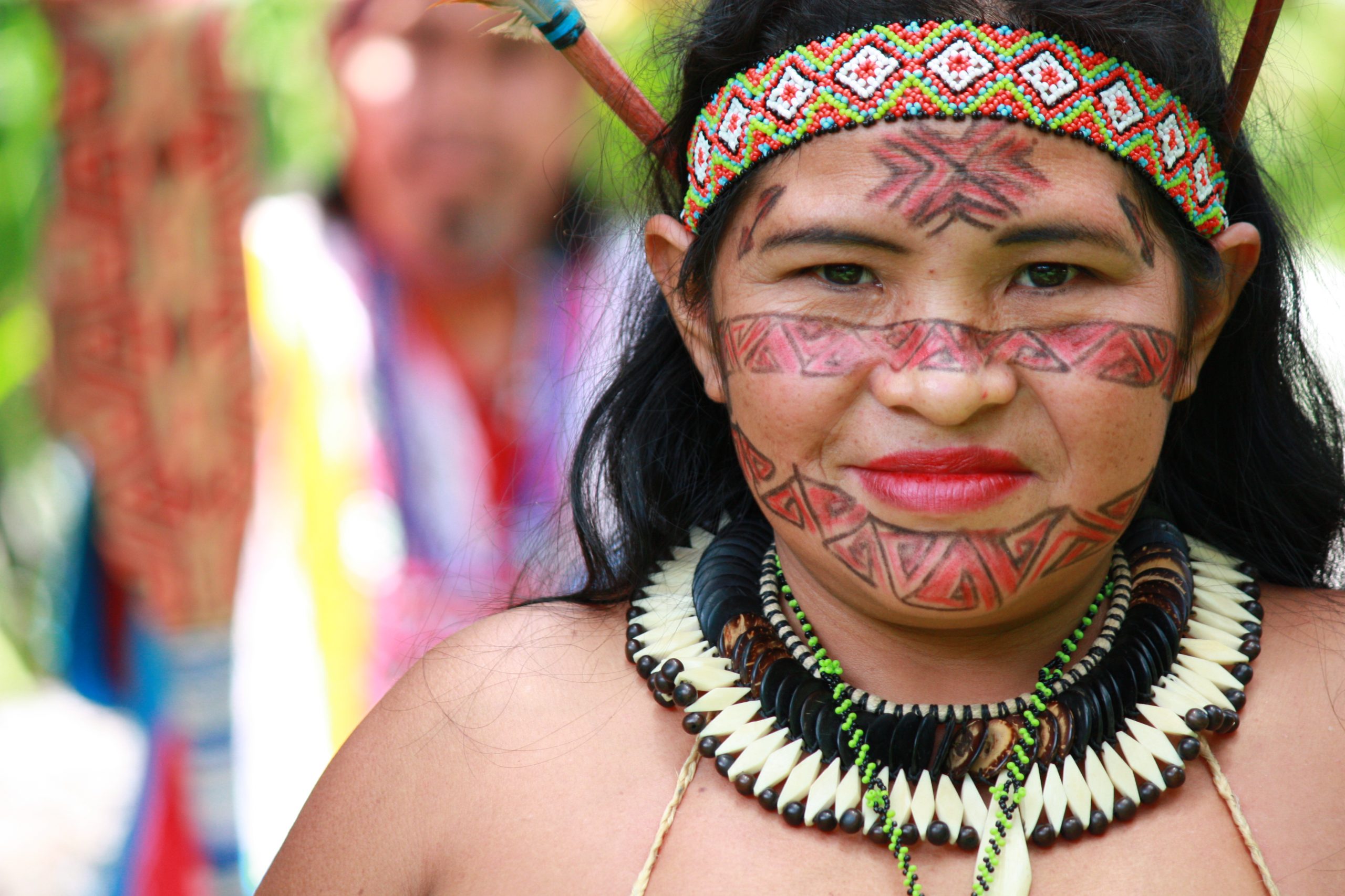 The image was made in a private wooded site in São Paulo, SP, Brazil - 1st November, 2011 with natives known as Katukinas, a South American tribe from Acre. An Indian Katukina woman is standing in front of a landscaping, her face  painted with urucum and she wears ethinic clothing. There´s an Indian man  unfocused at the background.